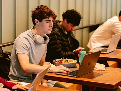 Student works on laptop while eating inside