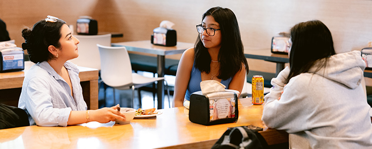 Three friends enjoy their meals sitting down inside